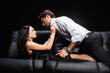 © LIGHTFIELD STUDIOS - side view of passionate woman unbuttoning shirt of young man on leather sofa isolated on black