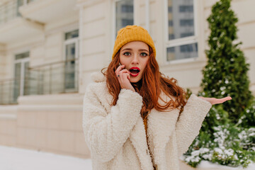 Wall Mural - Winsome lady with dark wavy hair talking on phone in cold day. Winter portrait of amazing ginger girl.