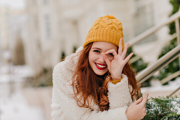 Wall Mural - Merry female model having fun in winter. Pleased caucasian ginger woman laughing on nature background.