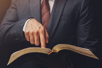 Wall Mural - man in suit pointing a text on an open bible on a black background