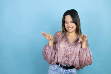 Beautiful latin woman wearing a pink shirt over blue isolated background disgusted expression, displeased and fearful doing disgust face because aversion reaction. Annoying