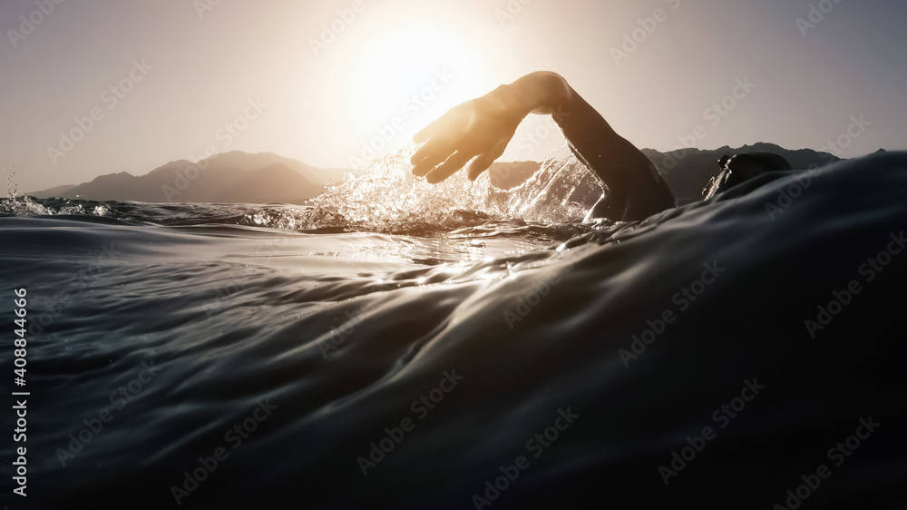 Athletic young man swimming at sea. Professional triathlon swimmer in ocean water. Young man athlete practicing at open water - obrazy, fototapety, plakaty 