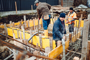 Construction details - worker laying and pouring cement or concrete with automatic pump in wooden casings foundation