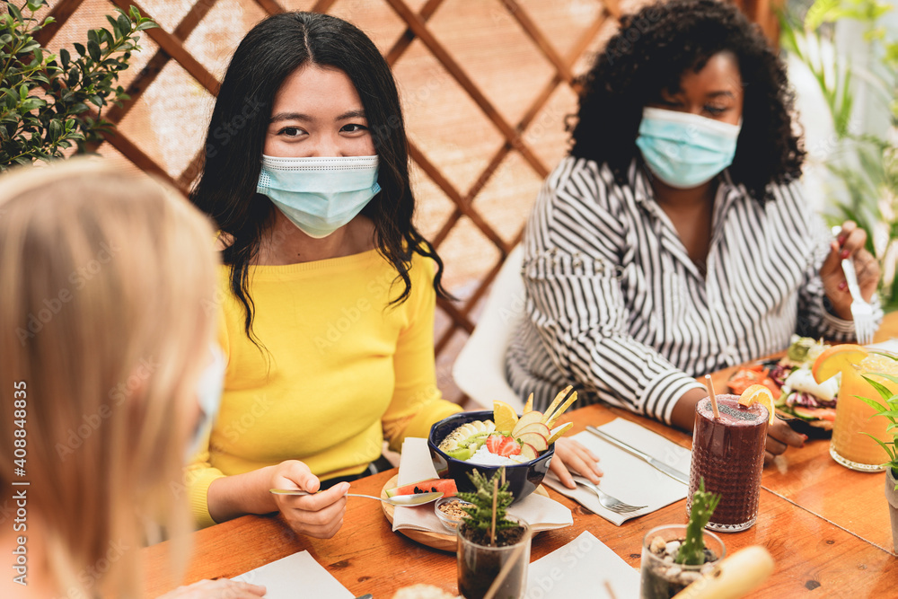 Young multiracial women enjoy brunch at bar while wearing surgical face mask for coronavirus outbreak - obrazy, fototapety, plakaty 