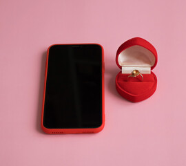 New smartphone and engagement ring in red gift box on pink background. The concept of best gift for Valentine's Day, birthday, International Women's day and other holidays. Copy space