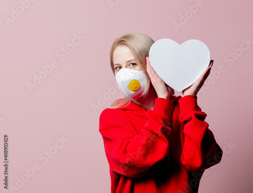 Woman in FFP2 anti-dust standart face mask hold heart shape banner on pink background