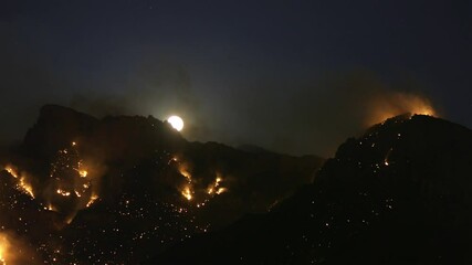 Wall Mural - Timelapse of Moon Above Hills in Uncontrolled Wildfire. Burning Land, Moonlight and Smoke. Climate Change and Air Pollution Concept