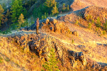 mature male tourist stands on the top of Akbura mountain and raised his hands up from a beautiful view of the Ural mountains at the autumn sunset.