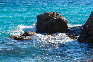 Wall Mural - Turquoise sea stone beach, breaking waves in bright sunlight. Colorful bright sea background. The concept of summer, vacation, travel. The purest clear sea water, large stones on the beach close-up