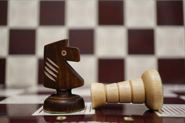 Close-up shot of a black wooden Knight next to a white fallen Rook on the chess board