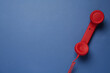 Red corded telephone handset on blue background, top view. Hotline concept