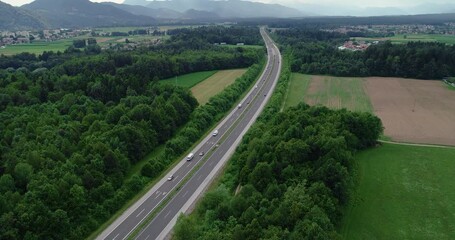 Wall Mural - Elevated view of traffic on highway in Slovenia. High flying drone over motorway, forest and green farming fields. Alps mountains in the distance. Tilt up