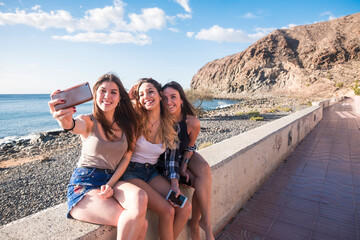 Group of three woman in friendship taking selfies and using phone near the beach on vacation - summer outdoor leisure activity for modern people have fun together with cellular