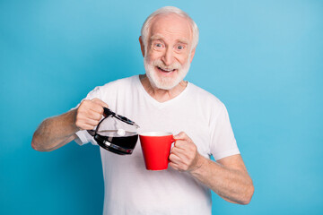 Wall Mural - Photo portrait of retired man pouring coffee in red mug isolated on pastel blue colored background