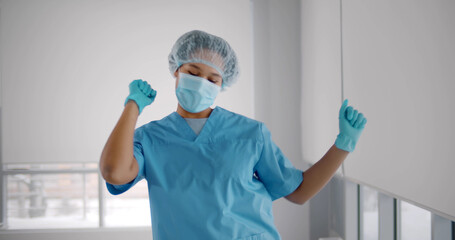 Young african american woman wearing scrubs uniform, gloves and mask dancing in hallway