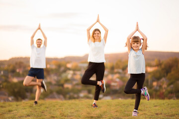 Wall Mural - Sporty healthy active family of three do sport exercises together outdoor at sunset. Focus on little girl