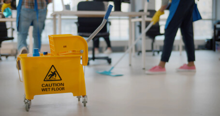 Janitor taking detergent spray from yellow cart to clean office windows