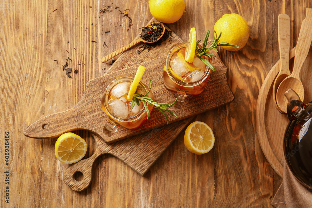 Mason jars of cold black tea with lemon on wooden background
