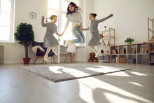 Happy family having fun at home. Overjoyed young woman and children enjoying free time and playing together. Excited mother and daughters jumping and laughing in cozy sunlit living-room of modern flat