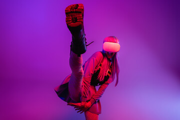 Poster - flexible and amazed young woman in virtual reality headset stretching on blurred purple background