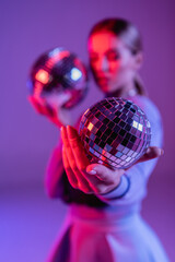 Poster - shiny disco ball in hand of trendy woman on purple and blurred background