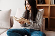 © Drobot Dean - Young happy woman reading book while sitting on sofa