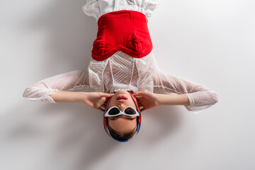 Wall Mural - top view of trendy woman in headscarf and sunglasses lying while looking at camera on white