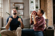 © JustLife - Two young friends enjoying at home. Men drinking beer and watching sports game on tv.