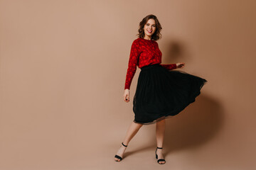 Full length view of slim girl in black skirt. Well-dressed caucasian woman dancing on brown background.