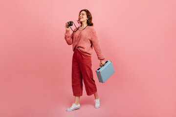 Sticker - Full length view of female tourist with camera. Studio shot of amazed woman holding blue valise.