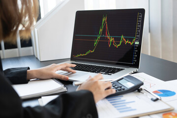 woman using a calculator and a laptop to calculate the company's financial results On the wooden table in the office and business work background, tax, accounting, statistics and analytical research