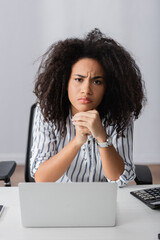 Wall Mural - displeased african american woman looking at camera near laptop