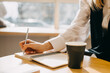 © Bostan Natalia - Closeup of a woman sitting at a table with a cup of coffee, writing down ideas in a notebook.