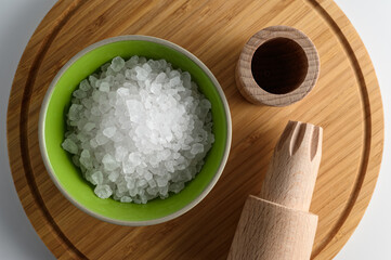 Porcelain bowl full of sea salt and small salt mill on wooden cutting board with white background