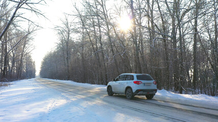 White car fast riding through snow covered icy road. SUV going at empty countryside route in winter forest on sunny day. Auto moving through scenic landscape way. Travel concept. Top view Drone shot