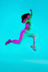 Wall Mural - Free. Brunette woman's portrait on blue studio background in mixed neon. Beautiful model jumping high, flying with hair blowed out. Concept of human emotions, facial expression, sales, ad, fashion.