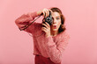 © Look! - Emotional young lady taking pictures. Studio shot of brunette woman with camera isolated on pink background.