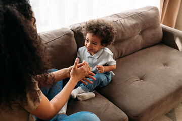 Wall Mural - Son and mother sitting on a sofa in living room and playing