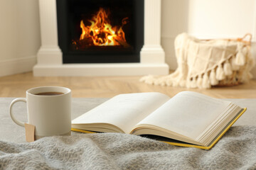 Sticker - Cup of hot tea and book near fireplace at home. Cozy atmosphere