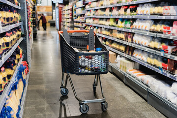 Shopping trolley near shelves with groceries in supermarket