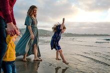 Laughing Girl In Blue Dress Jumping In Ocean Surf With Family Watching