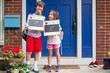 © Cavan Images - Two siblings stand together on stoop holding First Day of School signs