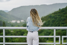 Back Side Of A Young Woman With Blonde Braided Hair Wearing A Denim Jacket And White Jean Resting On A Dam On A Rainy Day