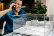 © Cavan Images - Mature man with a beard talking on the phone and looking at a model of a building. Architecture concept