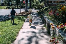 Two Young Boys Running On A Sidewalk In Neighborhood