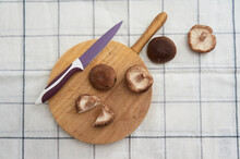From Above, The Raw Mushrooms Are Placed On A Wooden Cutting Board Next To A Lilac-colored Knife On A White Striped Cloth