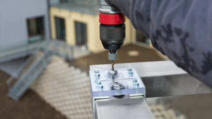 Closeup of drilling holes using a jig bushing for precise guide of twist drill bit. Boring template of acrylic and aluminum. Assembly stainless steel handrail to terrace railing in apartment building.