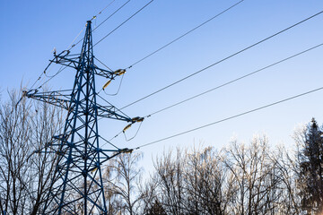 Canvas Print - steel transmission tower of high voltage power line and sunlit iced tops of frozen trees in city park on cold winter day