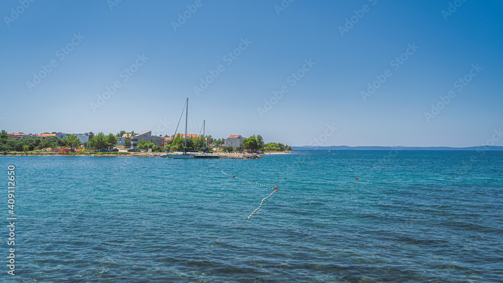 Yachts or sailboats moored at clear waters of Zaton bay with rocky coastline. Houses or resorts at the edge of turquoise water of Adriatic Sea Croatia