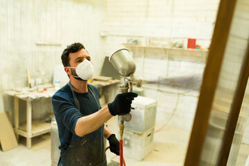 Attractive male carpenter painting a door with a spray gun